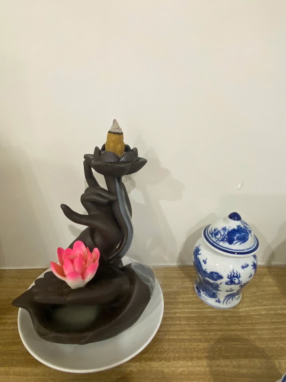 Bàn trầm hương hình bàn tay nâng đóa sen và hũ sứ men lam trên bàn gỗ — không gian tĩnh lặng trong nhà ngày đầu tháng