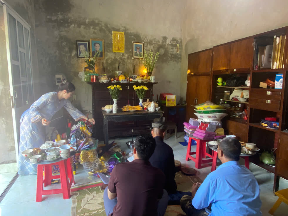 Lễ an tại gia trước bàn thờ gia tiên với các di ảnh, mâm cỗ, hoa cúc vàng và vàng mã, người thân quây quần khấn lễ