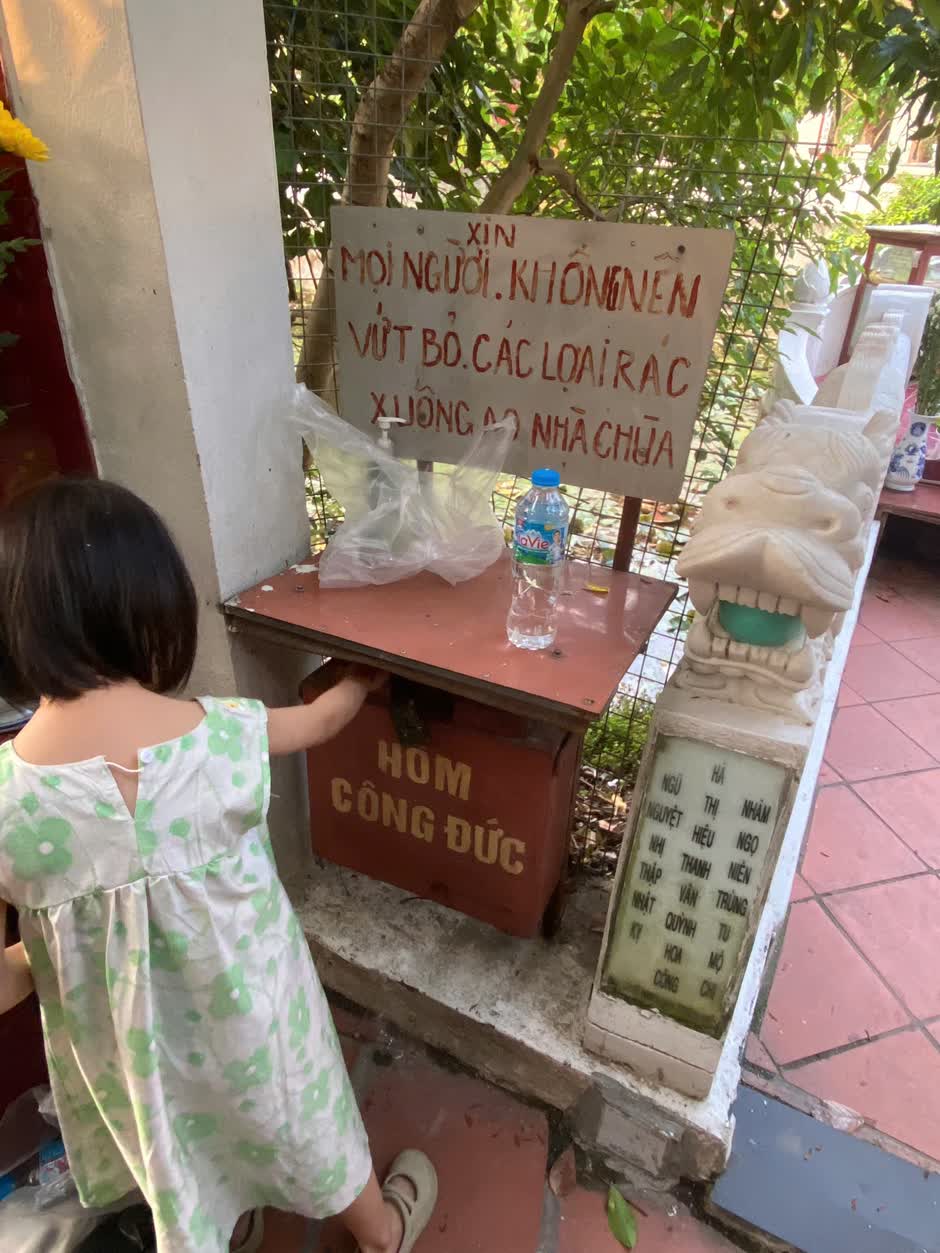 Một em nhỏ đứng bỏ tiền vào hòm công đức bên tấm bia đá khắc tên phần mộ tổ tiên trong khuôn viên chùa
